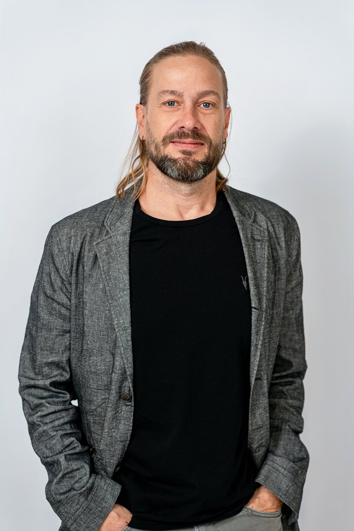 Three-quarter studio portrait in a dark shirt and gray jacket