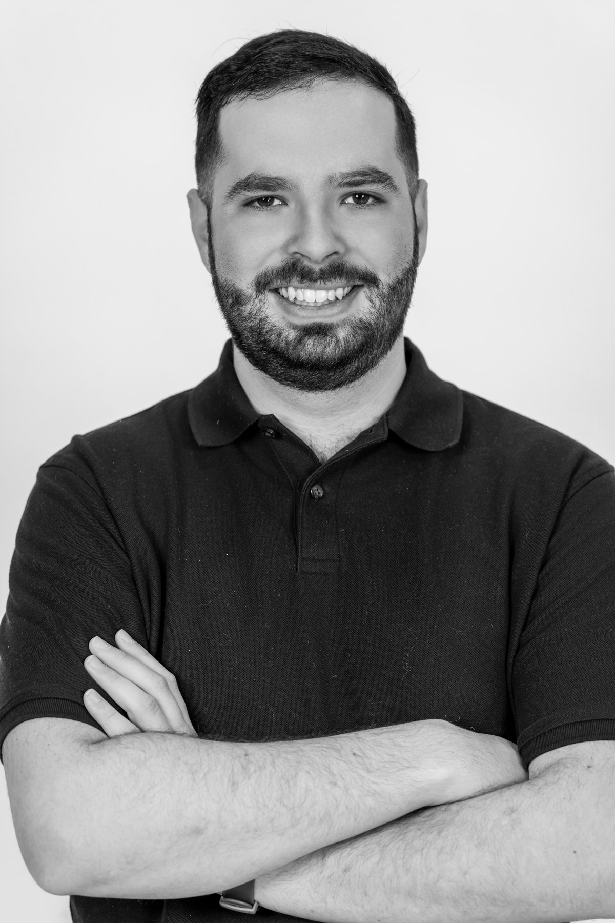 Black-and-white team portrait: smiling team member with a beard and folded arms