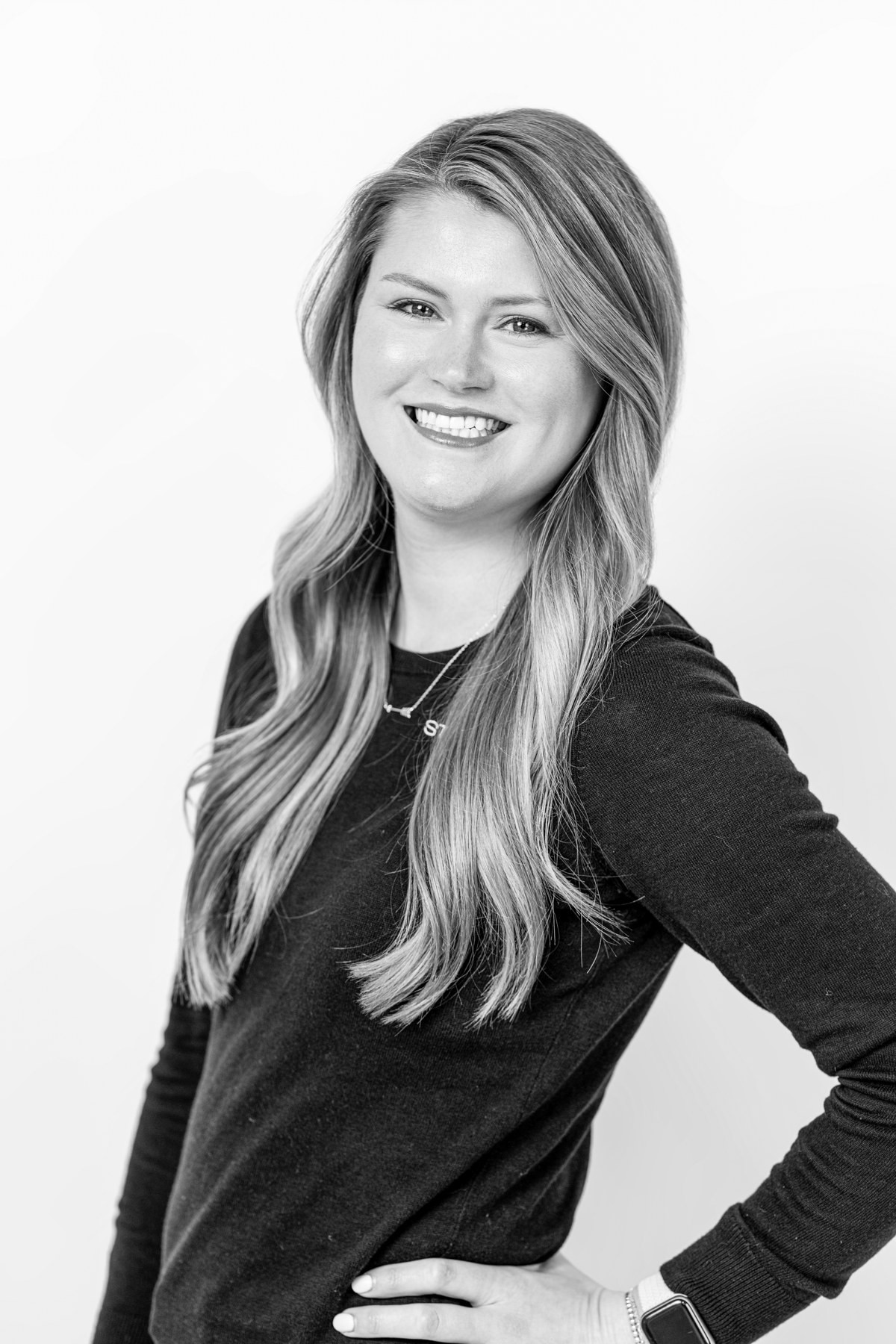 Black-and-white team portrait: smiling team member with long hair and a hand on the hip