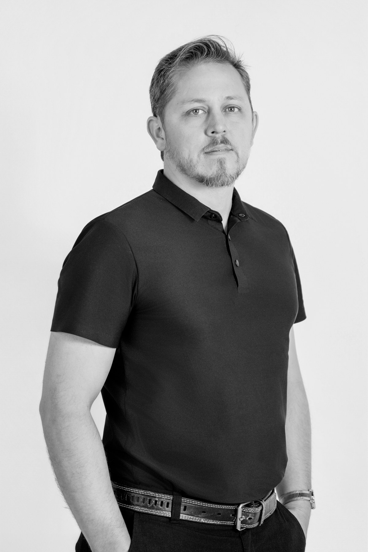 Black-and-white team portrait: team member standing upright in a plain dark polo