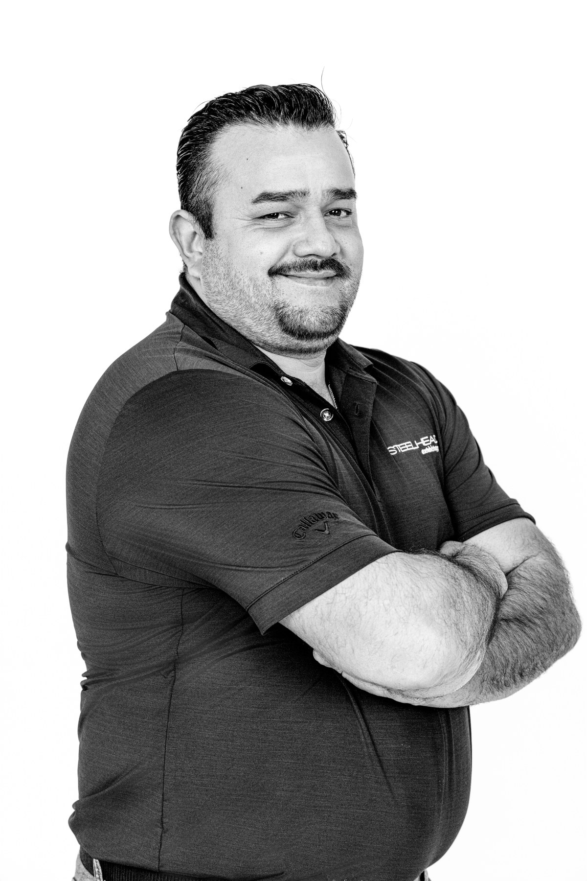 Black-and-white team portrait: smiling team member in a dark polo with folded arms