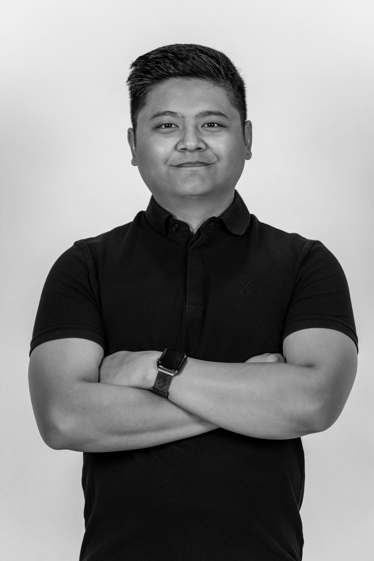 Black-and-white team portrait: team member in a plain dark polo with folded arms